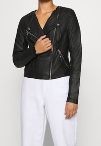 Giacca da moto in pelle nera con zip asimmetrica, colletto a bavero e maniche lunghe. Texture liscia con dettagli in metallo argentato.