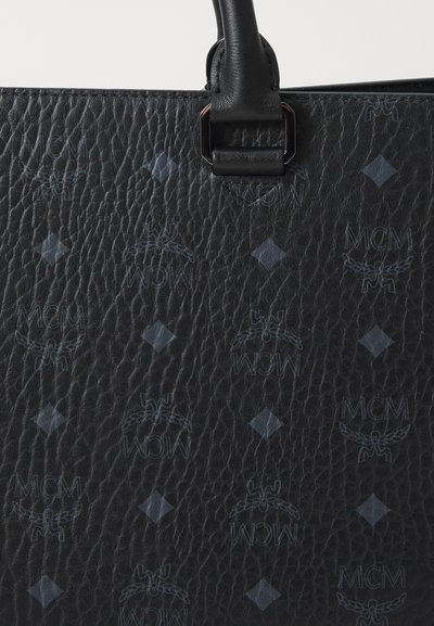 Svart läderväska med präglad MCM-logotyp, diamantmönster och strukturerad yta. Har robusta handtag och metallhardware-accenter.
