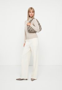 Pull à col montant beige, pantalons blancs à jambes larges et escarpins gris à bout pointu. Sac à main noir et beige à motif serpent. Textures simples et lisses.