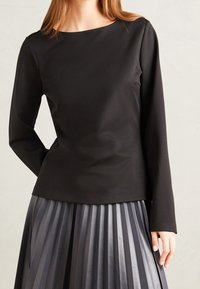 Haut noir à manches longues avec un col rond, associé à une jupe plissée grise au texture brillante et à des nuances variées.