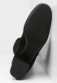 Botín de ante negro con suela lisa, tacón cuadrado y un logo sutil en la parte inferior. El diseño es elegante y minimalista.