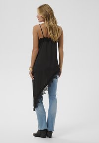 Schwarzes Satintop mit Spitzenbesatz, asymmetrischem Design, verstellbaren Trägern; kombiniert mit hellblauen Jeans und schwarzen Stiefeletten.