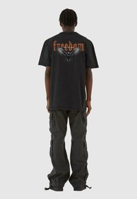 Sort oversized t-shirt med "freedom" tekst og ørnergrafik på ryggen. Båret med mørke cargo-bukser, der har lommer og snor.