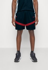 Sorte basketballshorts med en rød stribe langs kanten, prydet med et Bulls-logo. Båret med sorte træningssko og en mørk overdel.