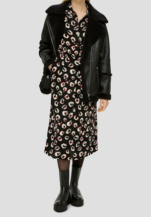 Woman wearing black shearling jacket over black midi dress with white and red animal print, black tights, and chunky black boots.