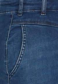 Mörkblå denimjeans med en framficka, synliga sömmar och en slät textur med en lätt urtvättad finish.