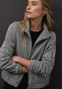 Šedá bomber bunda s rybí kostí vzorem, se zipem vpředu, vysokým límcem a elastickými manžetami; na rukávu má zipovou kapsu.