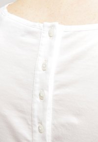 Gros plan d’un dos de chemise blanche avec cinq petits boutons ronds alignés verticalement le long de la couture centrale.