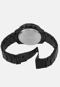 Črno metalno uro z povezanim pasom, ki ima izbočeno steklo in izrazito krono. Minimalistična zasnova z mat zaključkom.