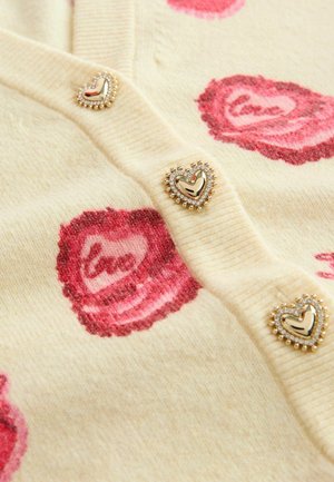 Lyse beige cardigan med lyserøde rosemønstre, pyntet med guldhjerteformede knapper omgivet af små rhinsten.