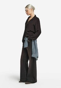 Chemise en soie noire avec col, associée à un pantalon en denim foncé à jambes larges et un foulard bleu clair texturé noué à la taille. Bottines gris clair doux.