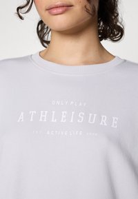 Sweatshirt gris clair avec un col rond, arborant un texte blanc indiquant "ATHLEISURE" et "ONLY PLAY" en évidence sur la poitrine.