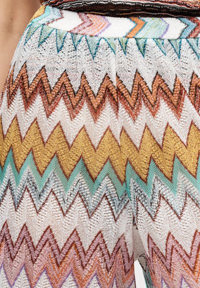 Κοντινό πλάνο πολύχρωμου πλεκτού υφάσματος με ζιγκ ζαγκ μοτίβα σε λευκούς, καφέ, κίτρινους, τυρκουάζ και πορτοκαλί τόνους σε ένα ένδυμα.