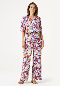 Bunt gemusterte Bluse und weiter Hosenanzug mit auffälligen Blumenmustern in Pink, Rot, Blau und Beige, aus leichtem Stoff gefertigt.