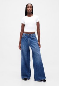 Modré džíny s širokými nohavicemi a vysokým pasem, s knoflíkovým zapínáním a vybledlou denní texturou, doplněné o přiléhavý bílý krátký rukáv top.