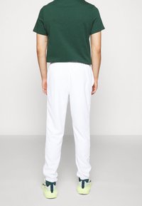 Grön kortärmad skjorta, vita joggbyxor med elastiska muddar och gröna sneakers med blå detaljer. Slätt tyg och avslappnad passform.