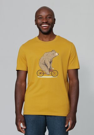Geel T-shirt met korte mouwen heeft een afbeelding van een beer die op een fiets rijdt. De stof lijkt zacht, met een ronde hals en een ontspannen pasvorm.
