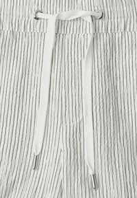 Tissu blanc à fines rayures verticales noires, avec un cordon blanc passé à travers des œillets métalliques à la taille.