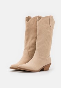 Beige suède cowboylaarzen met scherpe neuzen, decoratieve stiksels en een korte gestapelde hak. Gladde textuur met een klassiek westers design.