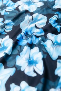 Cvetlični tekstil z modrimi in turkiznimi cvetovi na črni podlagi. Material ima gladko teksturo z rahlim sijajem.