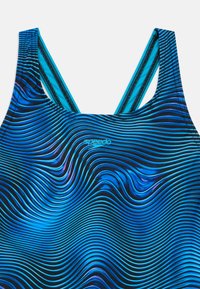 Μαγιό με σχέδιο κυμάτων, σε μαύρο και μπλε χρώμα. Κατασκευασμένο από ελαστικό υλικό με σταυρωτούς ιμάντες στους ώμους.