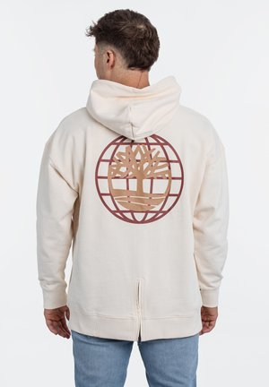 Cream hoodie features a large brown tree logo within a circular grid design on the back. The fabric appears soft with ribbed cuffs and a zipper detail.