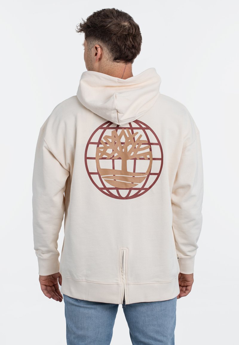 De crèmekleurige hoodie heeft een groot bruin boomlogo binnen een cirkelvormig rasterontwerp op de achterkant. De stof lijkt zacht met ribgebreide manchetten en een ritsdetail.