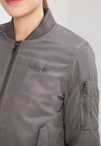 Grau Bomberjacke mit geripptem Kragen, Reißverschluss vorne und seitlichen Taschen. Verfügt über eine strukturierte Oberfläche und ein kleines gesticktes Logo.