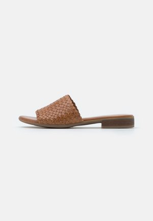 Brune vævet lædersandal med lav blokhæl, der har en glat fodseng og åbent tådesign. Minimalistisk æstetik med naturlig tekstur.
