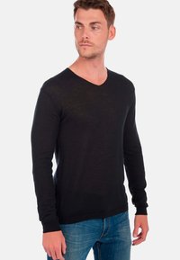 Schwarzer, langärmeliger V-Ausschnitt-Pullover aus leichtem Material, mit schmaler Passform und gerippten Bündchen, kombiniert mit blauen Jeans.