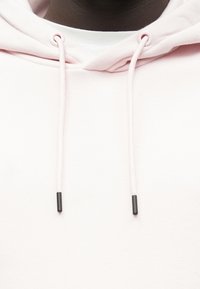 Hellrosa Hoodie mit Kordelzügen und schwarzen Plastikenden. Weiche Stoffstruktur, die ein minimalistisches Design ohne Muster zeigt.