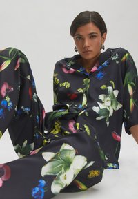 Zwart bloemenprint shirt en broek, versierd met kleurrijke bloemen zoals lelies en tulpen, gemaakt van een gladde, glanzende stof.
