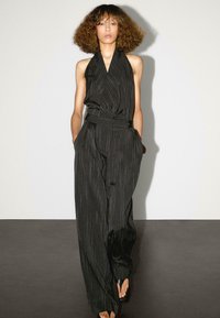 Svart halterneck jumpsuit med ränder, med figursydd midja, vida ben och sidofickor. Slätt tyg med en subtil glänsande yta.
