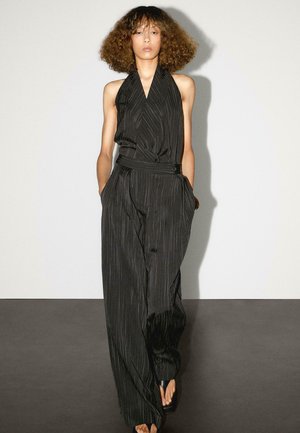 Sort halterneck jumpsuit med striber, der har en tætsiddende talje, brede ben og sidelommer. Glat materiale med en subtil glans.