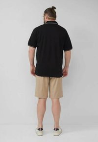 Schwarzes Polohemd mit weißen Akzenten, kombiniert mit hellbeigen Shorts. Der Stoff wirkt glatt; die Schuhe sind hell mit navyfarbenen Akzenten.