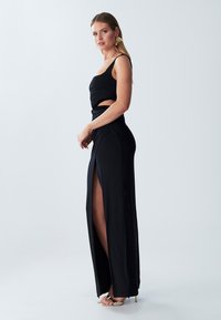 Black dress featuring a fitted bodice with ruching, cut-out waist, and a thigh-high slit, made of smooth fabric with a subtle sheen.