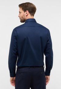 Camicia a maniche lunghe blu navy con colletto classico, texture liscia e polsi abbottonati. Presenta una vestibilità su misura e una leggera lucentezza.
