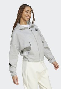 Γκρίζα φούτερ ζακέτα με φερμουάρ και μεγάλο γιακά, ελαφρώς φαρδιά εφαρμογή και μαύρες λεπτομέρειες logo. Διαθέτει ελαστικές μανσέτες και λεία υφή.