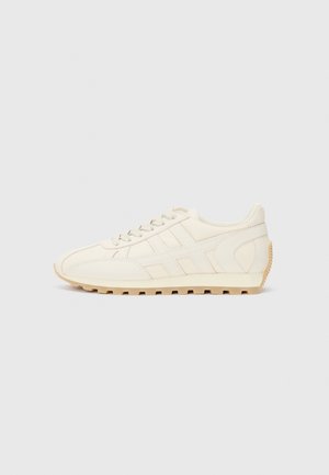 Cremefarbene Sportschuhe mit einem glatten Leder-Obermaterial, texturierten seitlichen Akzenten und einer kontrastierenden Gummisohle mit tiefen Rillen.
