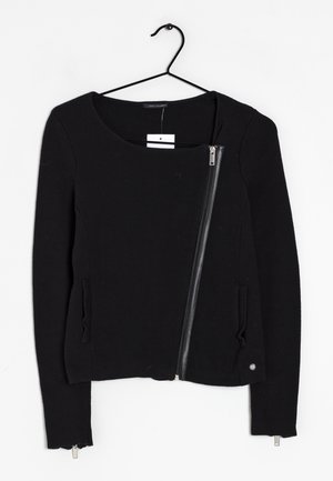 Musta pitkähihainen neulepaita, jossa on istuva leikkaus, diagonaalinen vetoketju, kaksi sivutaskua ja pyöreä pääntie.