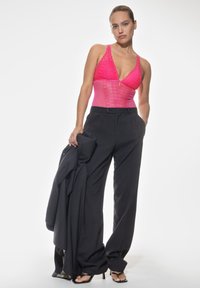 Fuchsia spetsbody med djup urringning, matchad med svarta högmidjade byxor och svarta klackar med öppen tå, hållande en jacka.