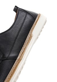 Scarpa slip-on in pelle nera con suola in gomma bianca e dettaglio in juta intrecciata lungo il bordo. Texture liscia con cuciture minime.