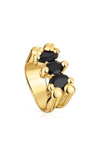 Anillo en tono dorado que presenta tres piedras negras facetadas, engastadas en acentos redondeados y con forma de burbuja sobre una banda lisa. Acabado pulido.