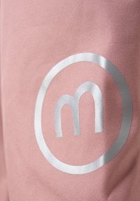 Lichtroze stof met een circulair zilveren logo waarin een gestileerde letter "m" is opgenomen. Gladde textuur met een subtiele glans.