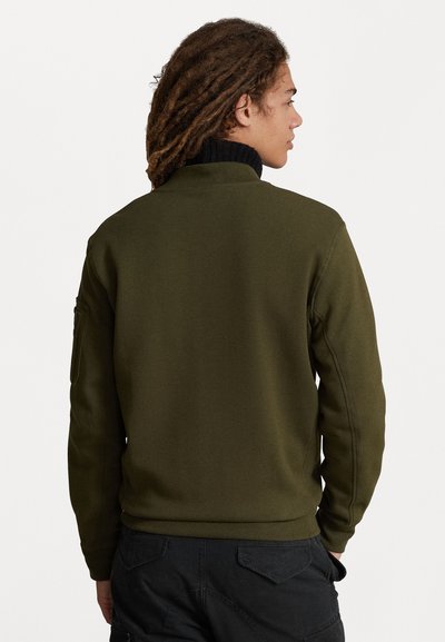Sweatshirt verde-oliva com gola alta preta. Apresenta uma textura suave e um bolso lateral na manga esquerda. Design simples e moderno.