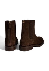 Bottines en suede marron avec des panneaux élastiques sur les côtés et une fermeture éclair à l'arrière, présentant une surface texturée et un petit talon robuste.