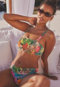 Šarena bikini kombinacija s uzorkom lista i cvijeća. Gornji dio ima kvadratni izrez i naboranu teksturu; donji dio ima dizajn s visokim strukom.