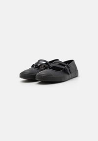 Sapatos pretos planos com tiras cruzadas, solas de borracha e um acabamento mate suave. Bico arredondado com sola texturizada para aderência.