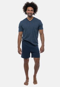 Marineblå V-neck T-shirt med lodrette hvide striber, parret med ensfarvede marineblå shorts, der har en afslappet pasform og blødt stof. Model barfodet.