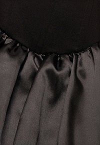 Vestito nero con corpetto aderente e cuciture verticali e gonna in raso arricciata. La texture liscia con finitura lucida contrasta con il corpetto.